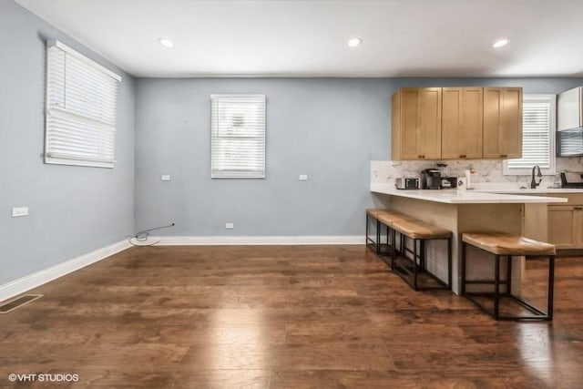 kitchen with dark wood-type flooring, sink, decorative backsplash, light brown cabinetry, and a breakfast bar area