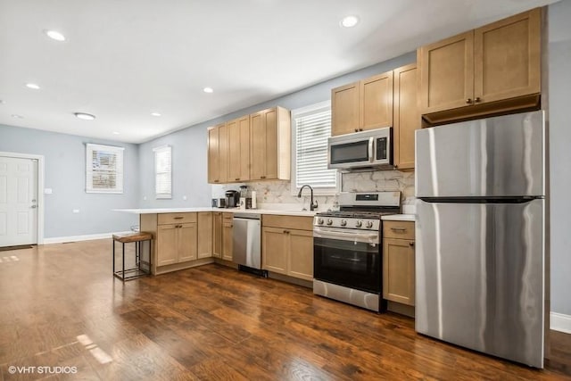 kitchen with kitchen peninsula, appliances with stainless steel finishes, decorative backsplash, a kitchen breakfast bar, and dark hardwood / wood-style floors