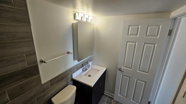 bathroom with vanity, toilet, and tile walls