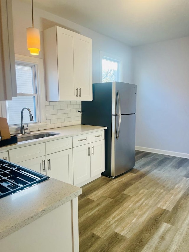 kitchen with sink, light hardwood / wood-style flooring, stainless steel fridge, decorative light fixtures, and white cabinets