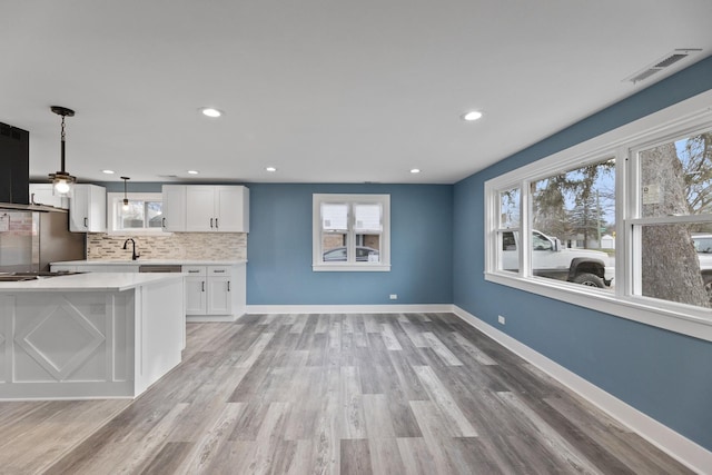 kitchen featuring white cabinets, light wood-type flooring, decorative light fixtures, and a healthy amount of sunlight