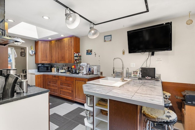 kitchen featuring backsplash, sink, a skylight, kitchen peninsula, and a breakfast bar area