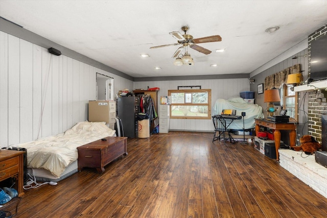 bedroom with wood walls, dark hardwood / wood-style floors, ceiling fan, and a fireplace