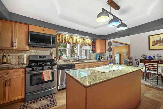 kitchen with sink, hanging light fixtures, stainless steel appliances, backsplash, and a kitchen island