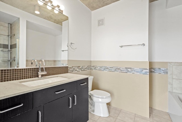 bathroom featuring vanity, tile patterned floors, toilet, tiled shower, and tile walls