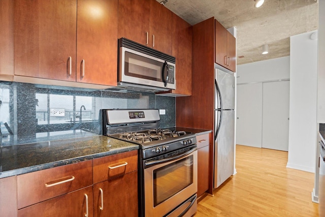 kitchen featuring dark stone counters, backsplash, appliances with stainless steel finishes, and light hardwood / wood-style flooring