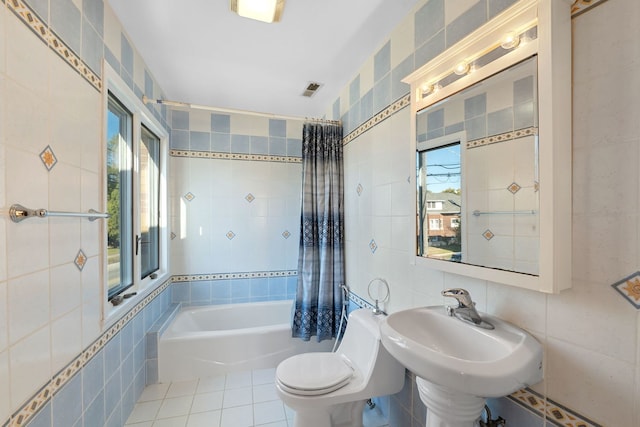 bathroom featuring toilet, tile patterned flooring, plenty of natural light, and tile walls