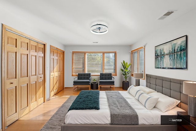 bedroom featuring light wood-type flooring, visible vents, and multiple closets