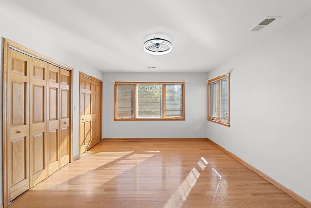 unfurnished bedroom with baseboards, light wood-style flooring, visible vents, and multiple closets