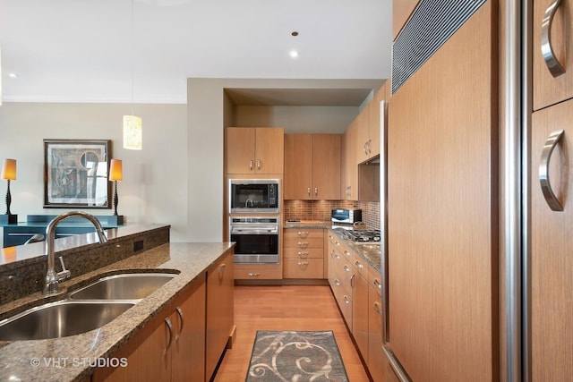 kitchen featuring dark stone counters, sink, built in appliances, decorative light fixtures, and light hardwood / wood-style floors