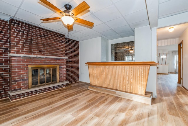 bar with a drop ceiling, a brick fireplace, and light wood-type flooring