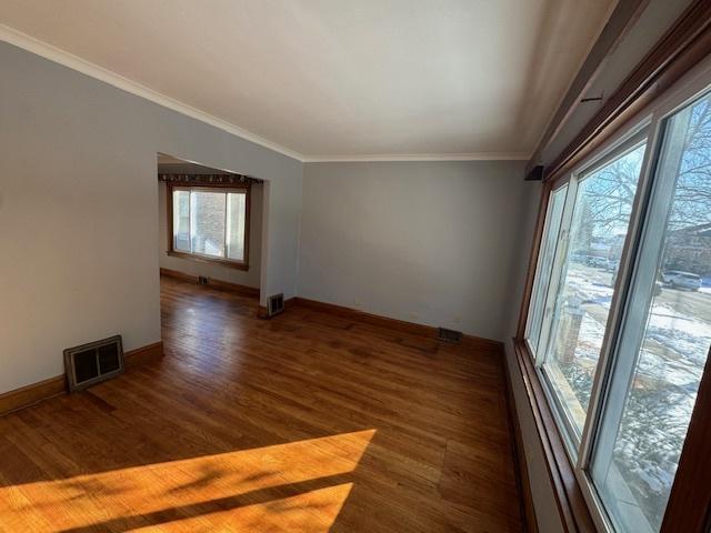 empty room with dark wood-style floors, visible vents, and crown molding