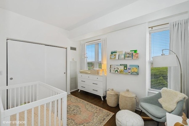 bedroom featuring dark wood-type flooring, a nursery area, and a closet