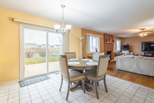 dining area featuring a brick fireplace, ceiling fan with notable chandelier, and light hardwood / wood-style flooring