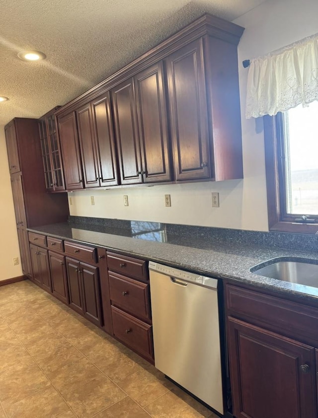 kitchen featuring a textured ceiling, a sink, stainless steel dishwasher, dark stone counters, and glass insert cabinets