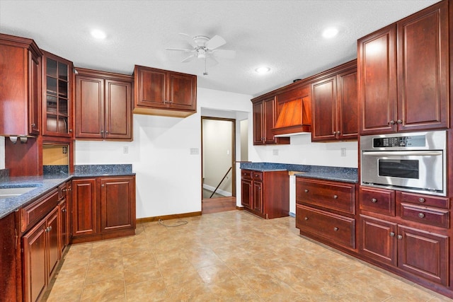 kitchen with custom exhaust hood, dark stone counters, oven, ceiling fan, and a textured ceiling