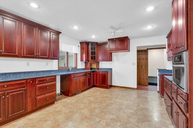 kitchen featuring ceiling fan, oven, a sink, dark brown cabinets, and dark countertops