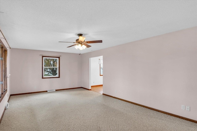 spare room featuring light carpet, visible vents, baseboards, ceiling fan, and a textured ceiling