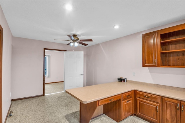 kitchen featuring light carpet, a peninsula, light countertops, built in study area, and brown cabinetry