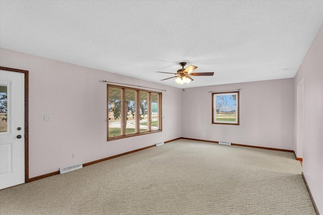 empty room featuring ceiling fan, light colored carpet, and a textured ceiling