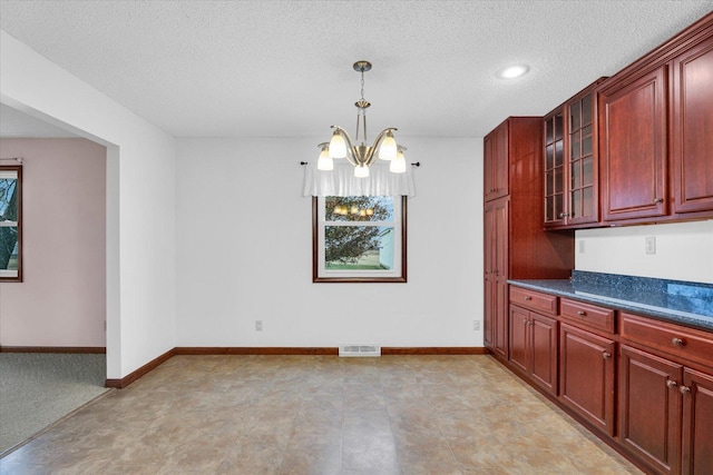 kitchen featuring visible vents, baseboards, reddish brown cabinets, dark countertops, and glass insert cabinets