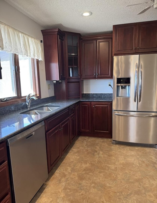 kitchen with light tile patterned floors, stainless steel appliances, glass insert cabinets, a sink, and a textured ceiling