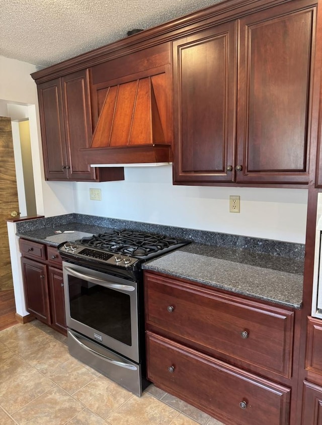 kitchen with stainless steel gas range, dark stone countertops, a textured ceiling, and custom exhaust hood