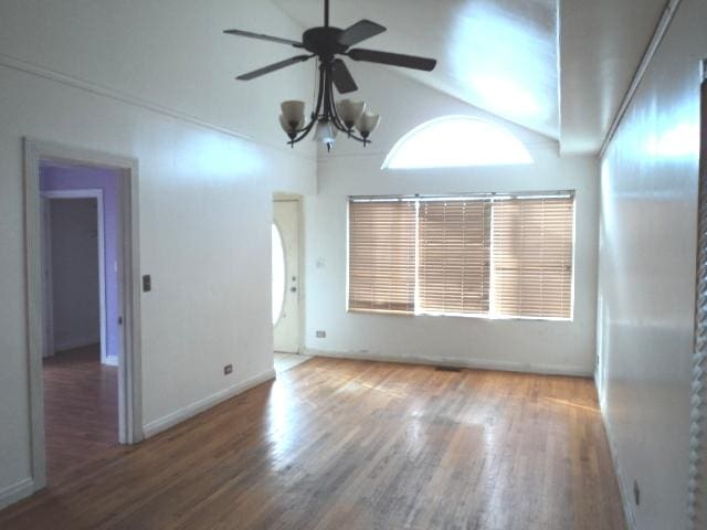 unfurnished room featuring ceiling fan with notable chandelier, dark hardwood / wood-style flooring, and vaulted ceiling