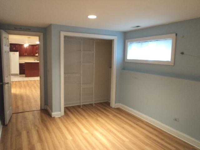 unfurnished bedroom with white fridge, light hardwood / wood-style floors, and a closet