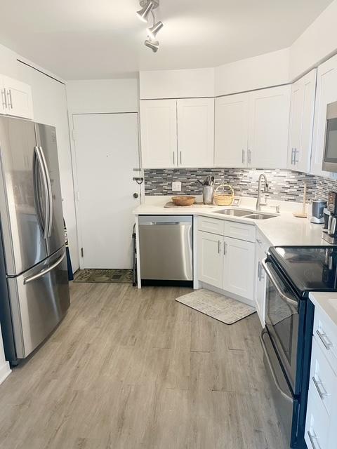 kitchen with tasteful backsplash, stainless steel appliances, sink, white cabinets, and light hardwood / wood-style floors