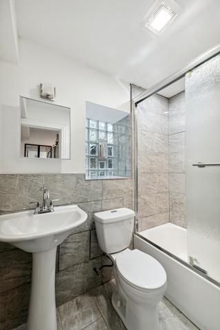 bathroom featuring shower / bath combination with glass door, tile walls, and toilet