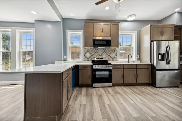 kitchen with plenty of natural light, tasteful backsplash, appliances with stainless steel finishes, and light hardwood / wood-style flooring