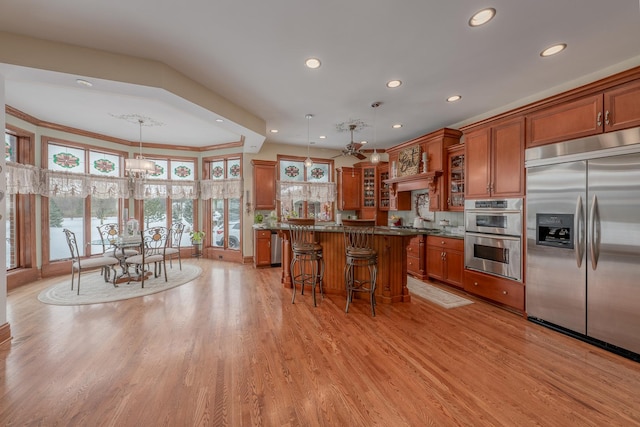 kitchen featuring stainless steel appliances, crown molding, decorative light fixtures, light hardwood / wood-style flooring, and a kitchen island