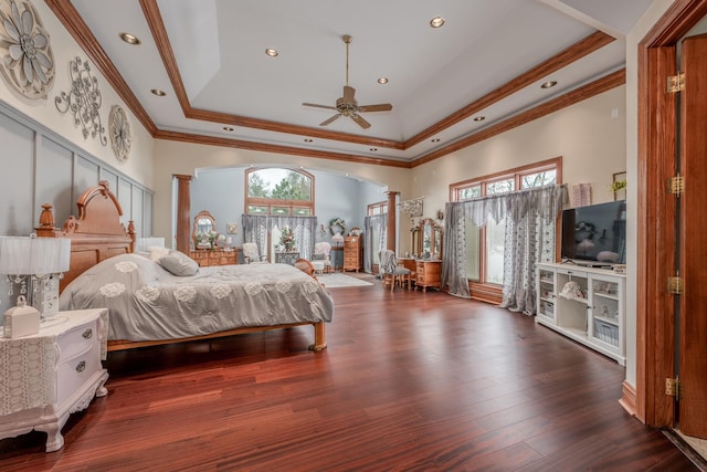 bedroom featuring ceiling fan, dark hardwood / wood-style flooring, decorative columns, crown molding, and a tray ceiling