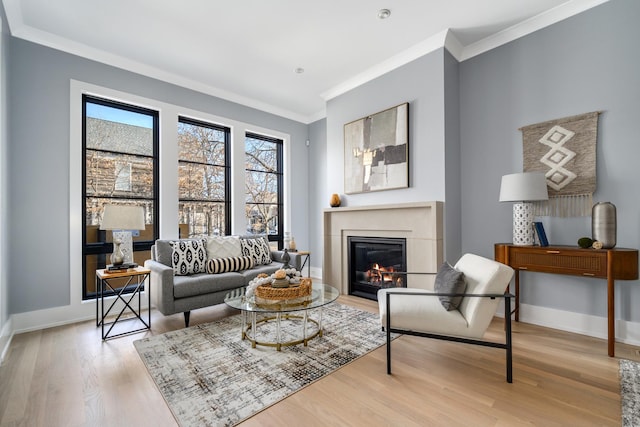 living area with a glass covered fireplace, baseboards, light wood-style flooring, and crown molding