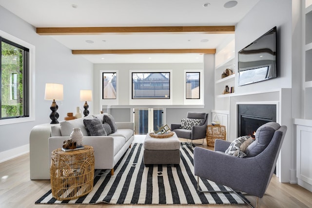 living area with beam ceiling, light wood-style flooring, baseboards, and a lit fireplace