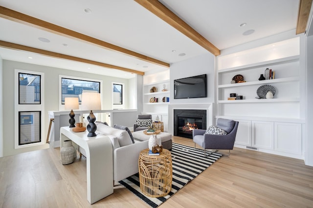 living room featuring beam ceiling, a glass covered fireplace, light wood-style flooring, and built in features