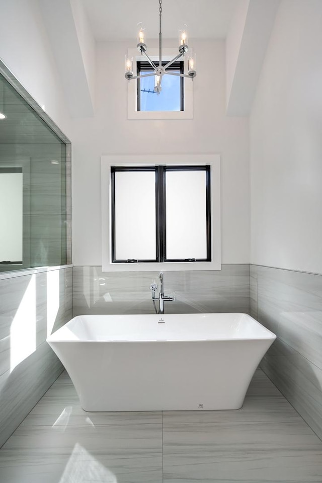 bathroom featuring tile walls, a notable chandelier, and a freestanding bath