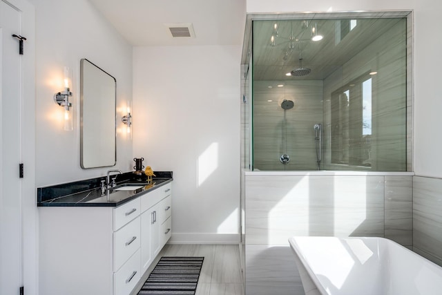 bathroom featuring visible vents, baseboards, tiled shower, a freestanding tub, and vanity