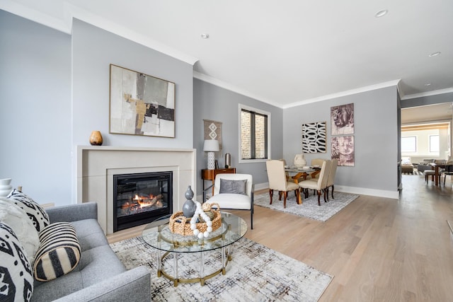 living room featuring a glass covered fireplace, baseboards, light wood-style floors, and ornamental molding