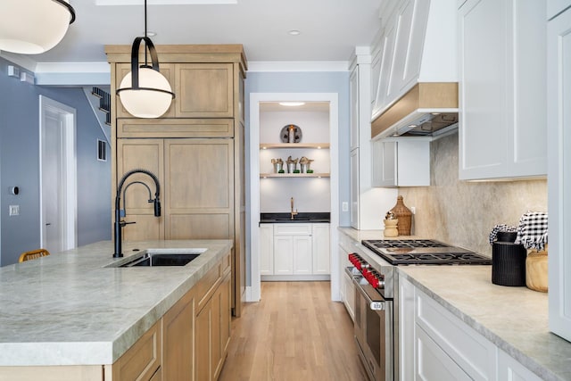 kitchen with light wood finished floors, an island with sink, custom exhaust hood, high end stainless steel range, and a sink