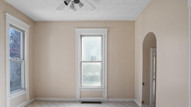 unfurnished room with arched walkways, a ceiling fan, and baseboards