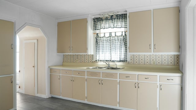 kitchen with cream cabinetry, arched walkways, light countertops, and a sink