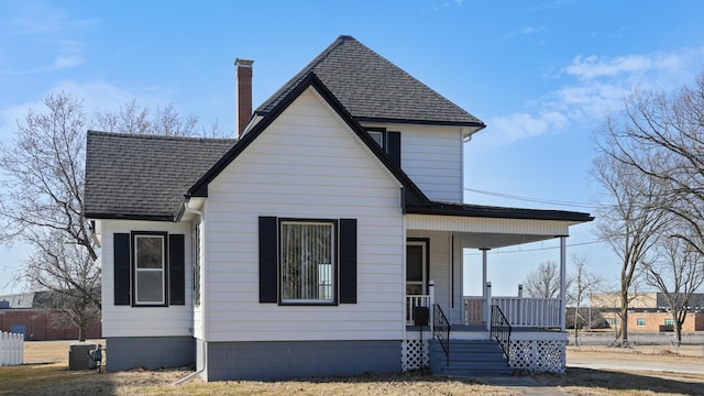 rear view of house featuring covered porch, a shingled roof, and a chimney