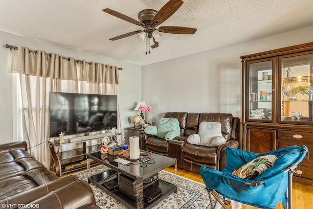 living room with ceiling fan, light wood-type flooring, and a textured ceiling