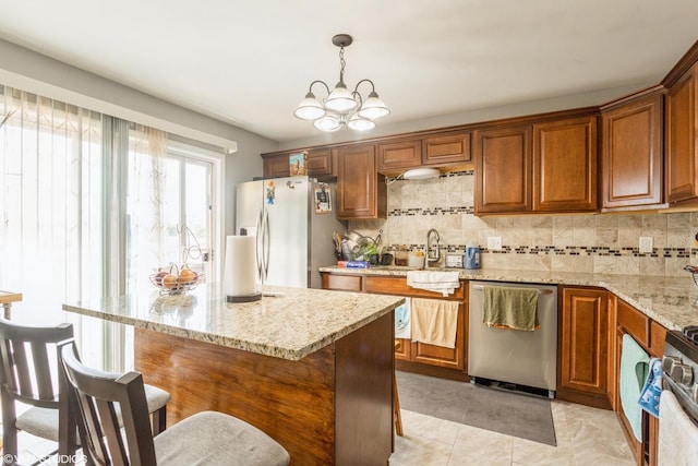 kitchen with light stone counters, stainless steel appliances, sink, pendant lighting, and a chandelier