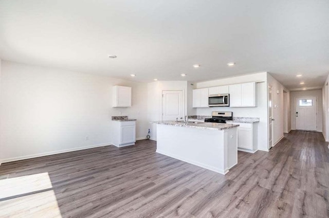 kitchen with light stone countertops, white cabinetry, an island with sink, light hardwood / wood-style floors, and appliances with stainless steel finishes