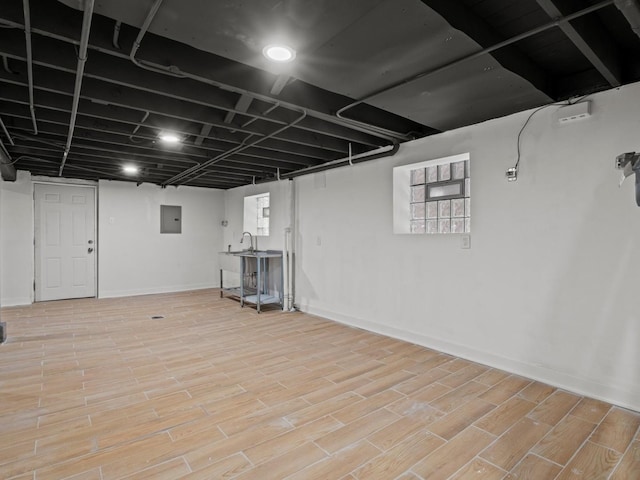 basement featuring plenty of natural light, electric panel, and light hardwood / wood-style flooring