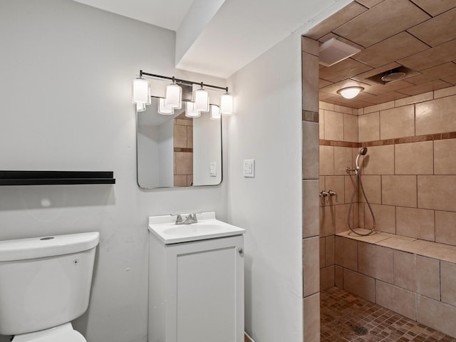 bathroom with a tile shower, vanity, and toilet