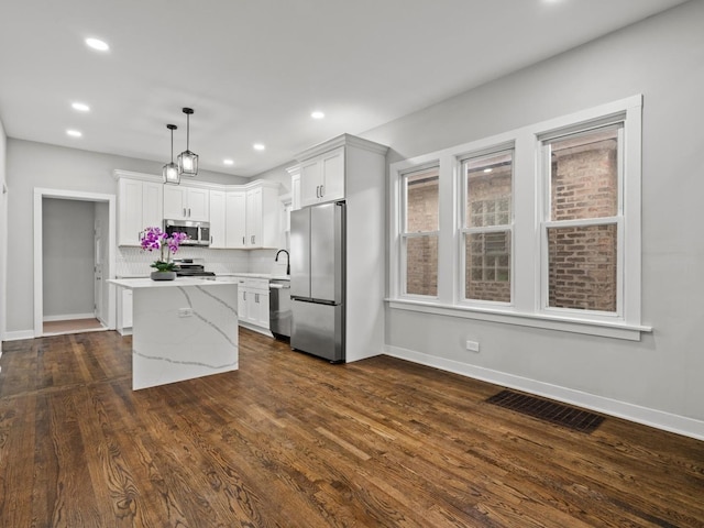 kitchen featuring appliances with stainless steel finishes, tasteful backsplash, dark wood-type flooring, white cabinetry, and hanging light fixtures